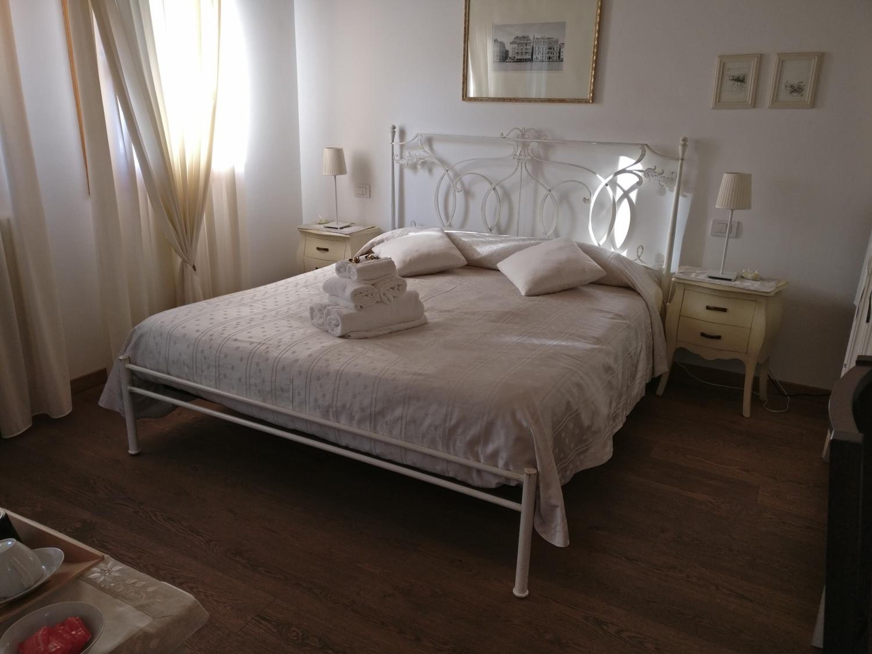 Une chambre à coucher bien rangée, avec un lit, des tables de chevet, une lampe et un tableau encadré au mur.