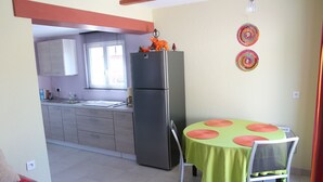 A compact kitchen with a refrigerator, a dining table with a green tablecloth, and a chair. - Small studio / Furnished rental (Neuwiller-lès-Saverne)