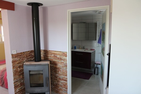 A room with a wood-burning stove, a brick wall, and a kitchen area with cabinets and a sink.