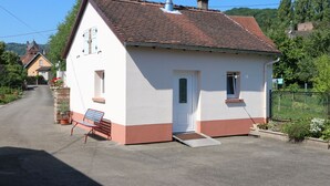 A small, single-story house with a sloped roof, a chimney, and a small porch with a bench. - Small studio / Furnished rental (Neuwiller-lès-Saverne)