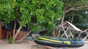 A green inflatable boat labeled "Fish Hunter" on a sandy beach with a wooden structure and a tree in the background. - Berakit Bay Resort (Bintan)