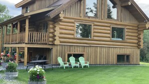 A log cabin with a balcony, large windows, and outdoor seating. - Sawinglogzz Log Cabin (Copper Center)