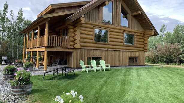 A log cabin with a balcony, outdoor seating, and a well-maintained lawn. - Sawinglogzz Log Cabin (Copper Center)