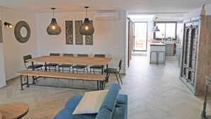 Moderni olohuone, jossa on ruokailutila. Tilaan kuuluu suuri puinen pöytä, sininen sohva ja riippuvalaisimet.