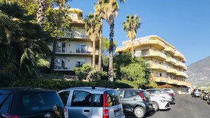 A multi-story residential building with balconies, parked cars, and palm trees. - Sanremo the enchanted refuge with panoramic terrace overlooking the sea (Sanremo)