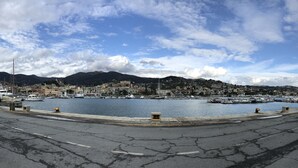 Un port avec des bateaux, une route longeant le rivage et un paysage urbain avec des bâtiments et des montagnes en arrière-plan.