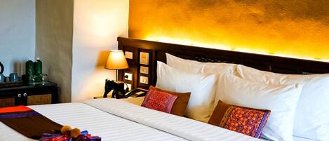 Habitación de hotel con una cama bien hecha, una mesita de noche con lámpara y un cabecero con luz cálida.