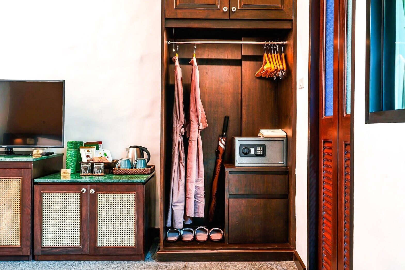 A compact room with a television, a small cabinet with toiletries, a shoe rack, and a coat hanging on a hook.
