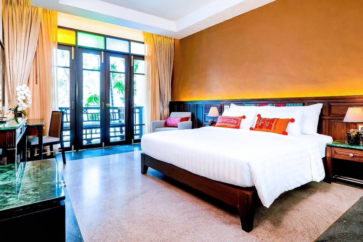 Une chambre d’hôtel avec un grand lit, un bureau, une chaise, une table de chevet et une vue sur l’extérieur grâce à une porte vitrée.