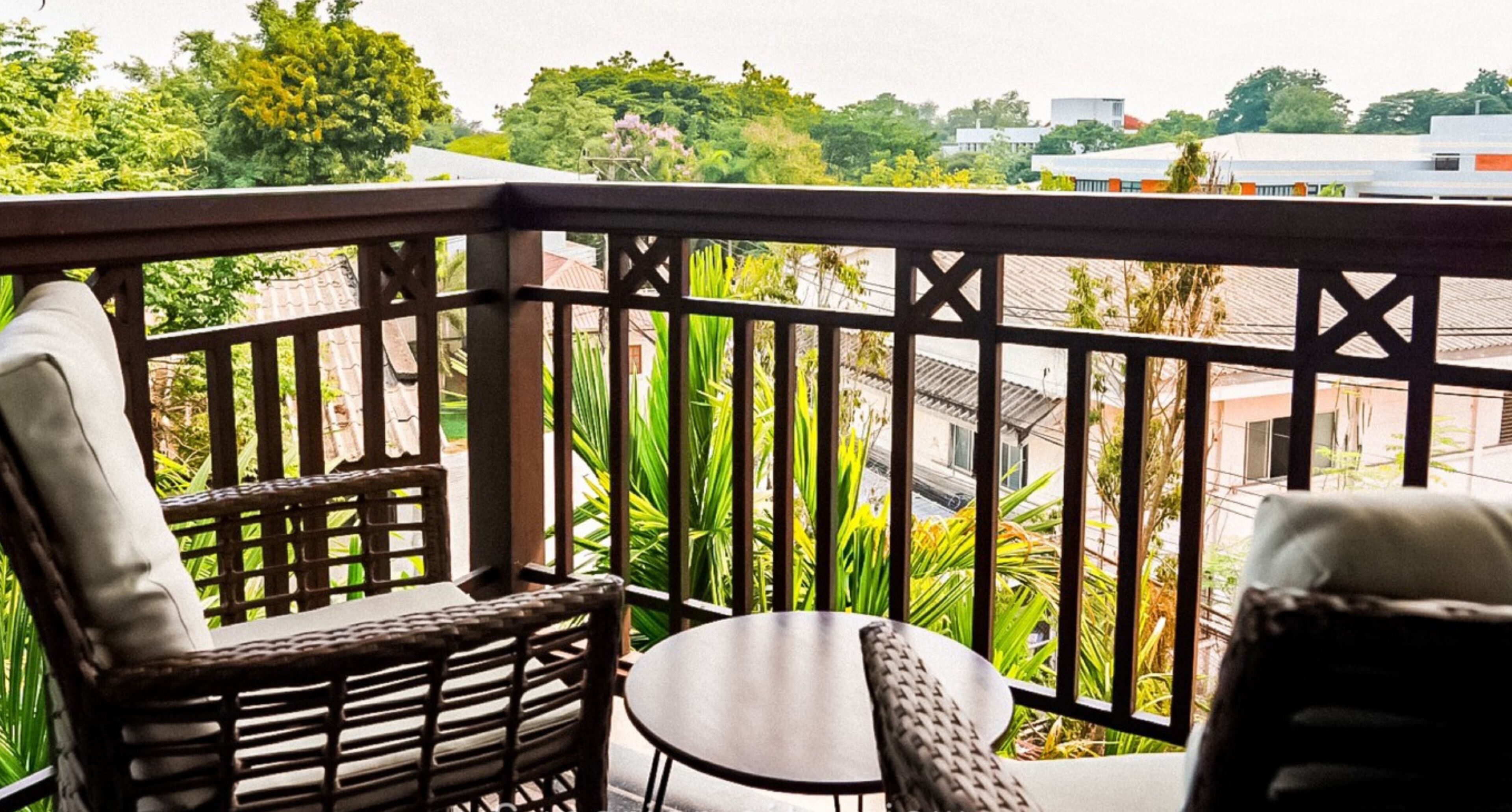 A balcony with wicker furniture and a view of greenery and buildings.