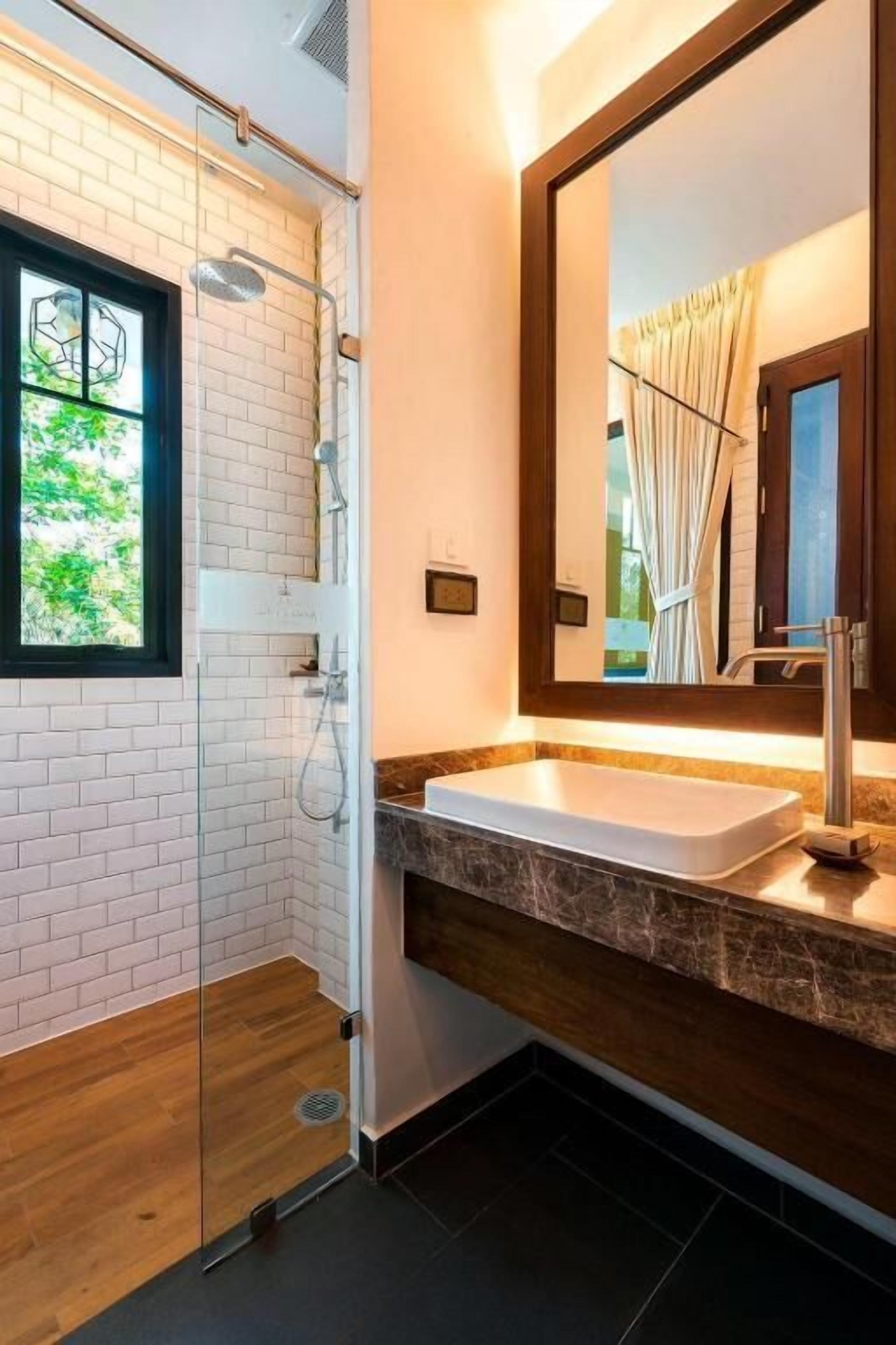 Un baño moderno con ducha de vidrio, lavabo blanco y un espejo grande.