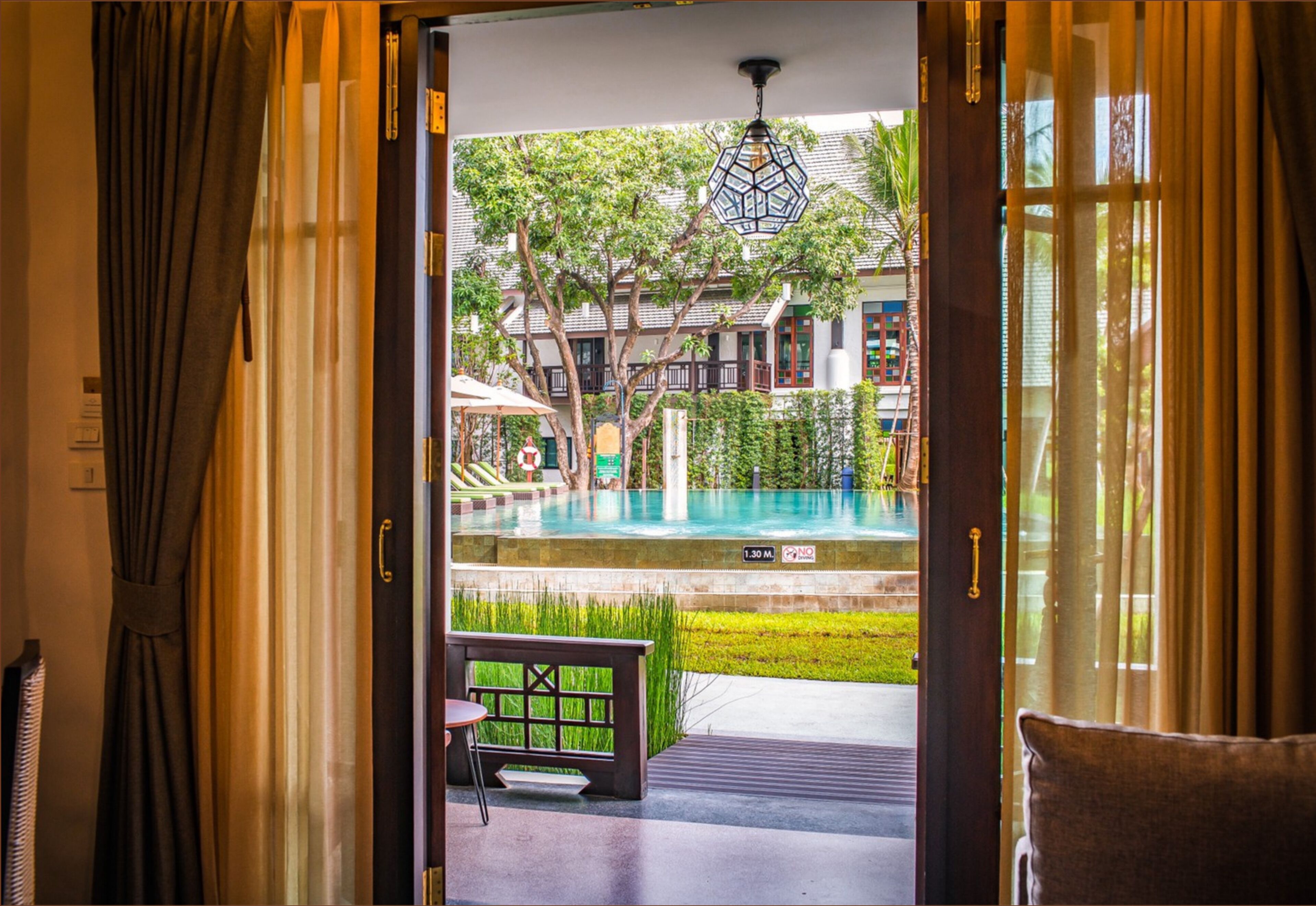 An open doorway leading to a pool area with a bench and umbrellas.