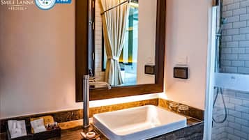 A bathroom with a white sink, a mirror, and a shower area. There are toiletries on the counter and a towel rack above the mirror.