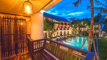 A poolside area with wooden benches and lounge chairs, a pool, and a building with multiple balconies and windows.