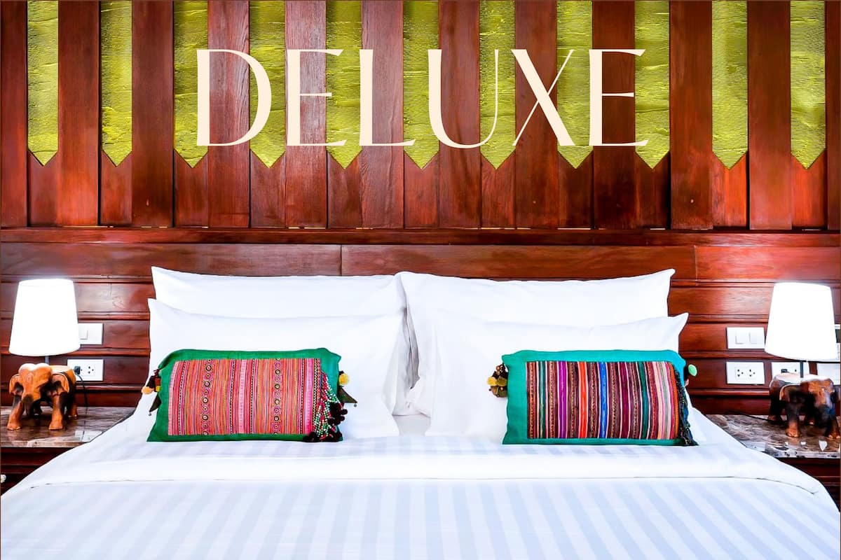Une chambre d’hôtel de luxe avec une tête de lit en bois, deux oreillers aux motifs colorés et un lit avec du linge de lit blanc.