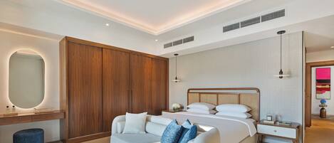 A modern hotel room with a large bed, a sofa, a vanity with a mirror, and a wooden wardrobe.