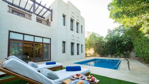 Un espace piscine extérieur moderne, doté de chaises longues et d’une table à manger où l’on peut prendre ses repas.