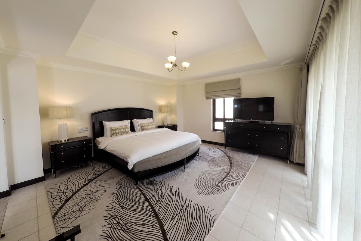 Un'ampia camera da letto con un grande letto, una TV a schermo piatto, una cassettiera e un tappeto decorato.