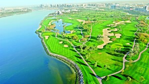 Un parcours de golf avec un plan d’eau d’un côté et, en arrière-plan, la silhouette d’une ville.