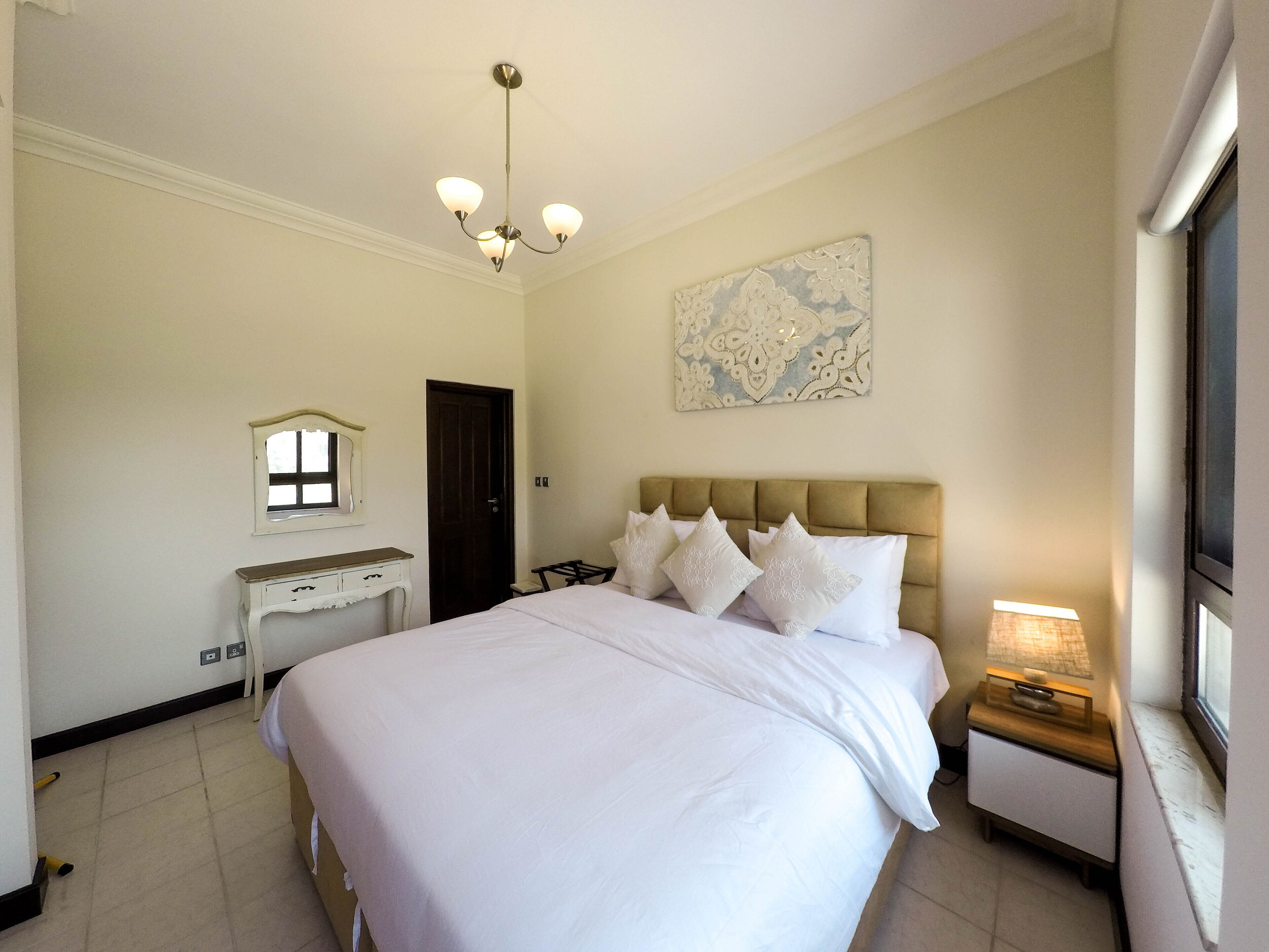 Une chambre à coucher avec un grand lit, une table de chevet, une commode, un bureau, une porte et une fenêtre.