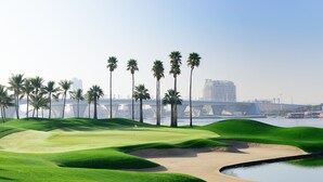 Un parcours de golf avec des bunkers de sable, des palmiers et un obstacle d’eau.