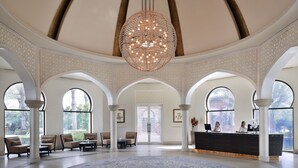 Un hall d’entrée spacieux, agrémenté d’un grand lustre décoratif, d’un comptoir de réception et de coins salon avec un tapis à motifs.