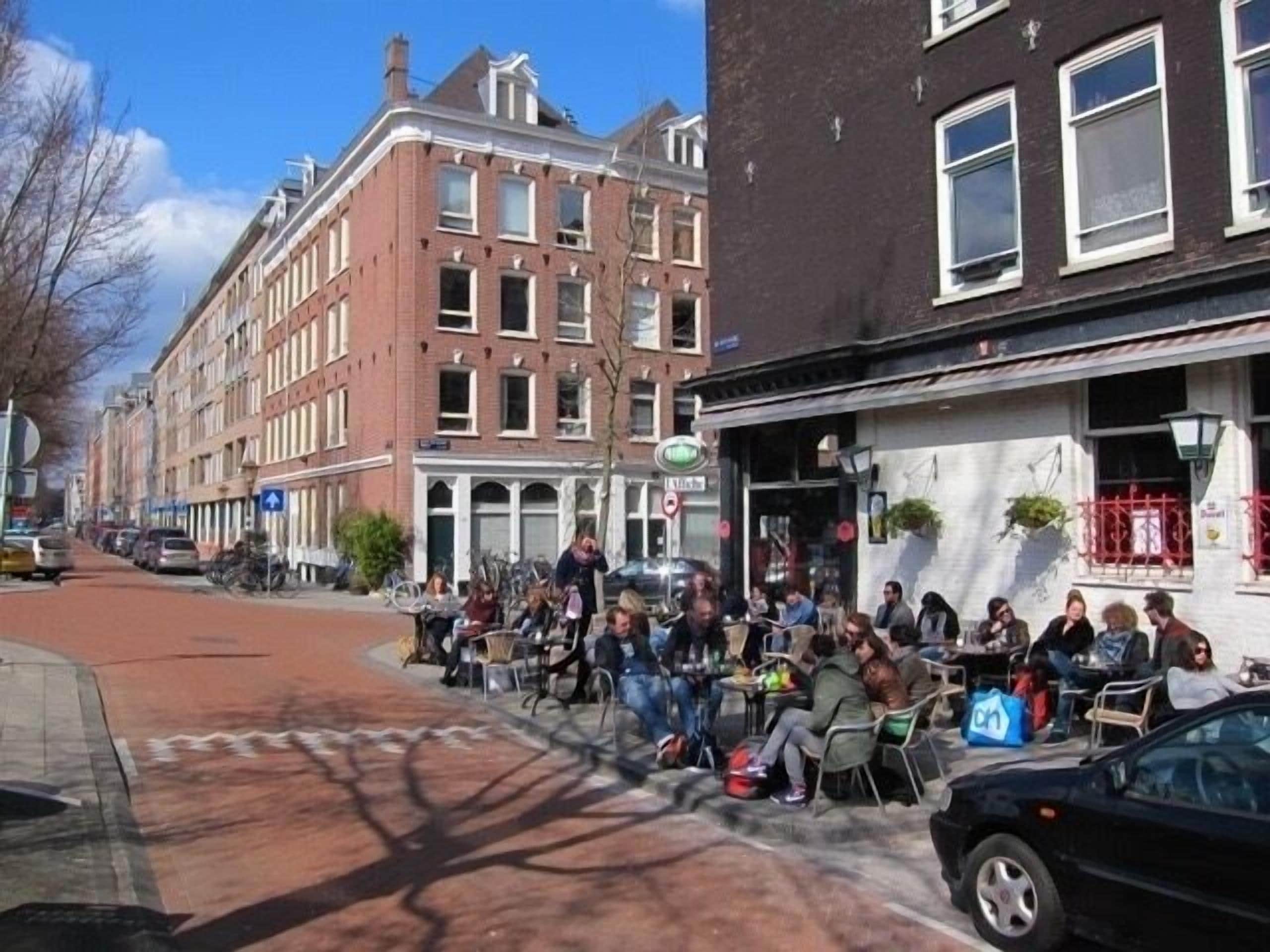 Une rue bordée de voitures garées et un groupe de personnes assises devant un immeuble.