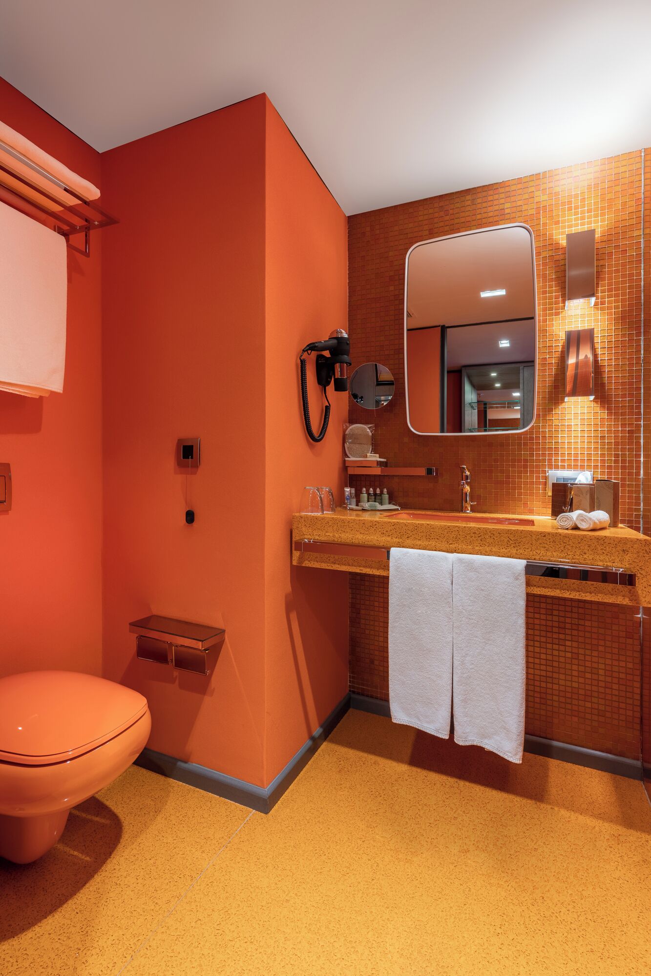 Un baño con inodoro rosa, un lavabo con espejo y un perchero para toallas.