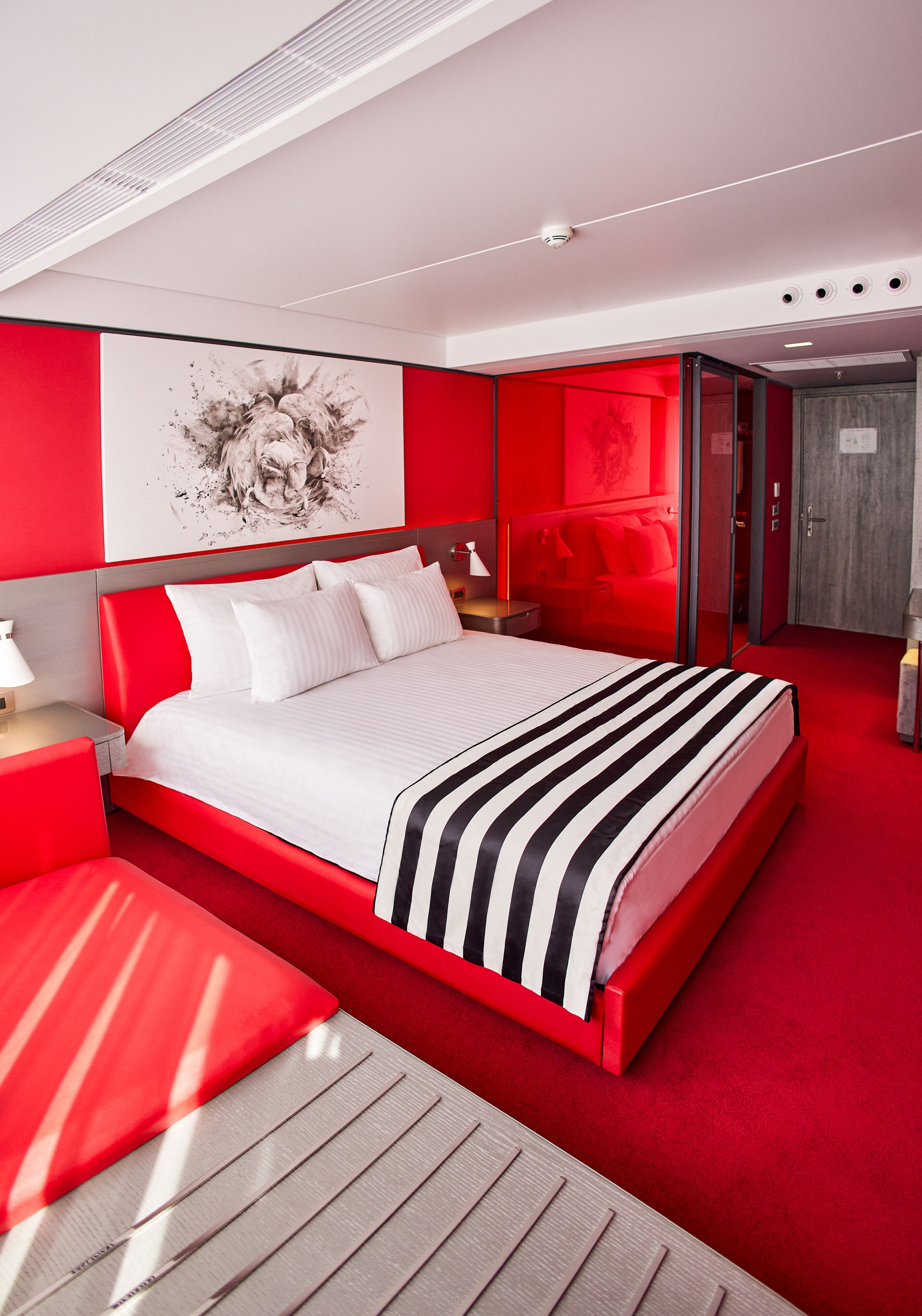 Una habitación de hotel moderna con una cama grande, detalles en rojo y una alfombra roja.
