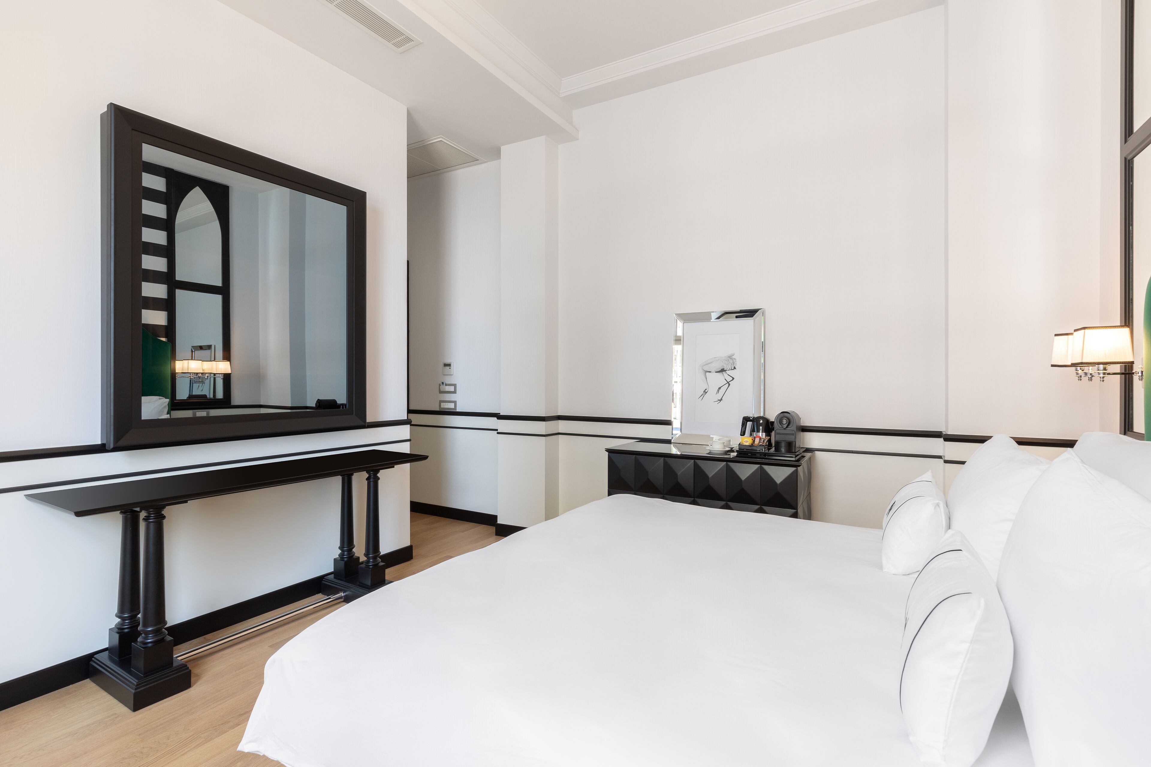 A hotel room with a large bed, a bedside table with a lamp, a mirror, and a small cabinet.