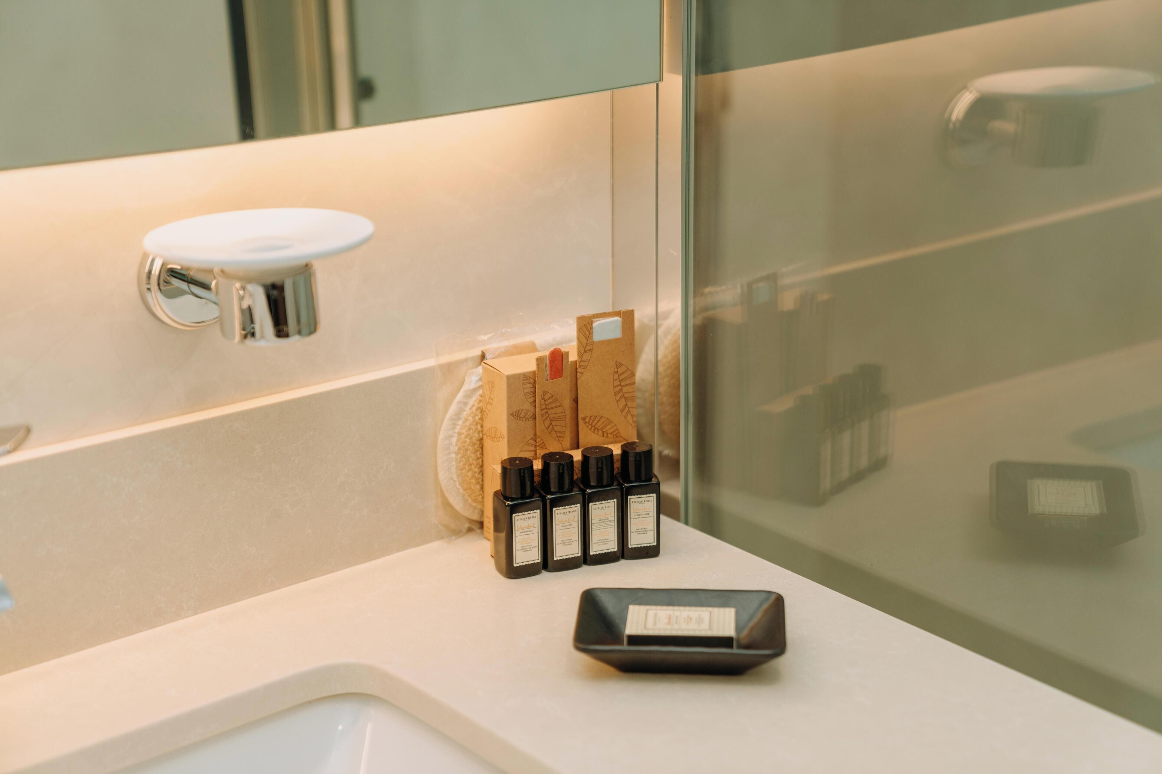 Casa de banho com lavatório branco, espelho e conjunto de artigos de higiene, incluindo dispensador de sabonete e suporte para escova de dentes.