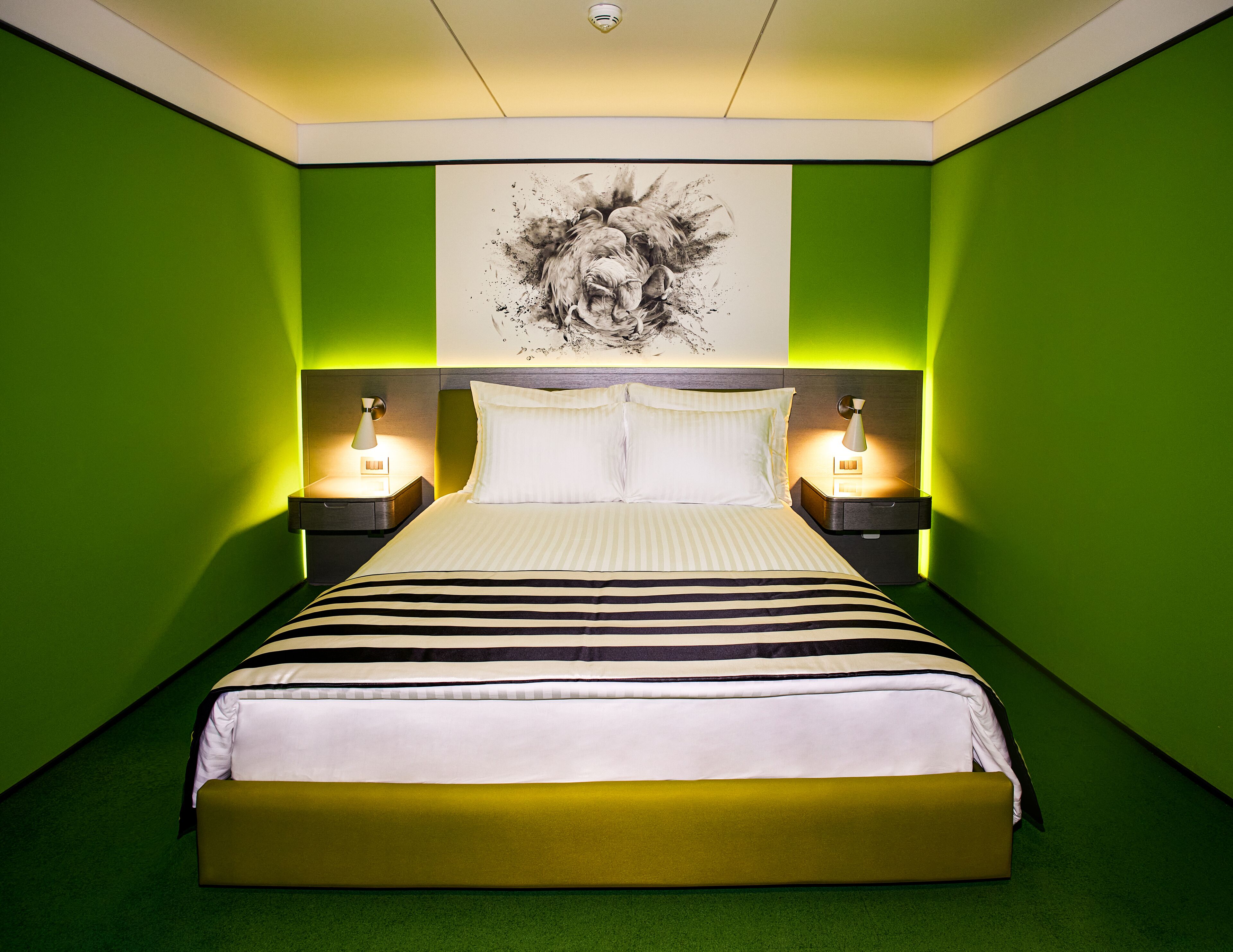 Un dormitorio moderno con paredes verdes, una cama grande con ropa de cama a rayas, dos mesitas de noche con lámparas y una lámpara en el techo.