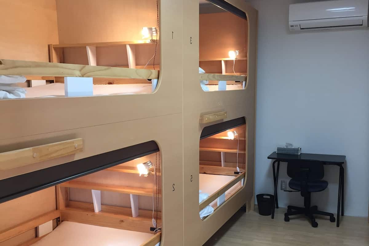 Habitación con literas, un escritorio, una silla, aire acondicionado y un cesto de basura.