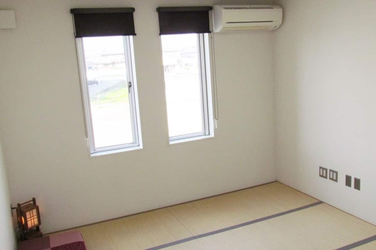 Una habitación con dos ventanas, aire acondicionado de pared y suelo de esteras de tatami.