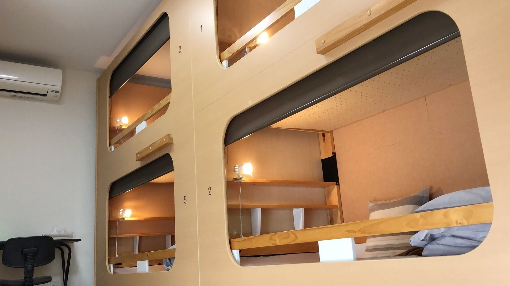 A dormitory-style room with bunk beds, a desk, and an air conditioning unit.
