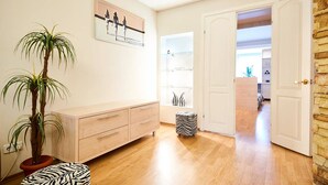 A hallway with a wooden floor, a light-colored wall, a potted plant, a zebra-patterned ottoman, a white door, and a shelf with decorative items. - Home-Hotel Mechnikova 7 (Kyiv)