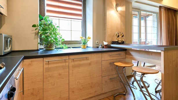A modern kitchen with wooden cabinets, a built-in stove, a window with blinds, and a bar area with stools. - Home-Hotel Mechnikova 7 (Kyiv)