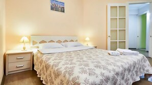 Un lit bien fait, recouvert d’une couvre-lit à motifs floraux, une lampe de chevet et une table de chevet avec des tiroirs.