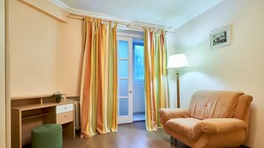 Une pièce comprenant un bureau en bois, un pouf vert, un fauteuil orange et une lampe.