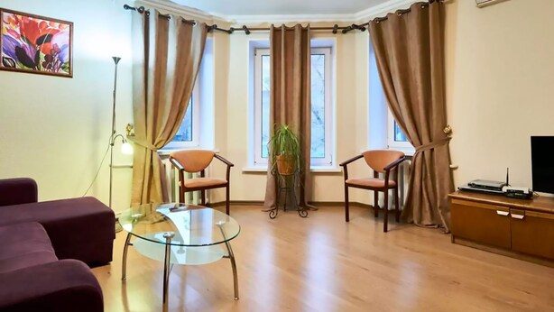 Un salon avec une table en verre, deux chaises, un canapé, une plante en pot et un téléviseur posé sur un meuble en bois.