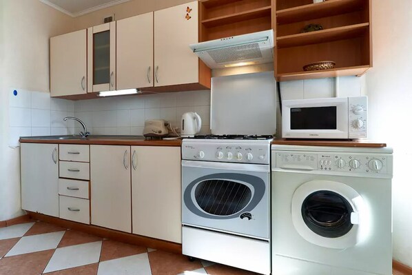 A compact kitchen with a stove, microwave, oven, and washing machine.