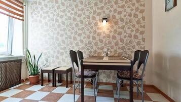 A dining area with a checkered floor, patterned wallpaper, a table with chairs, a potted plant, and a wall-mounted light fixture.