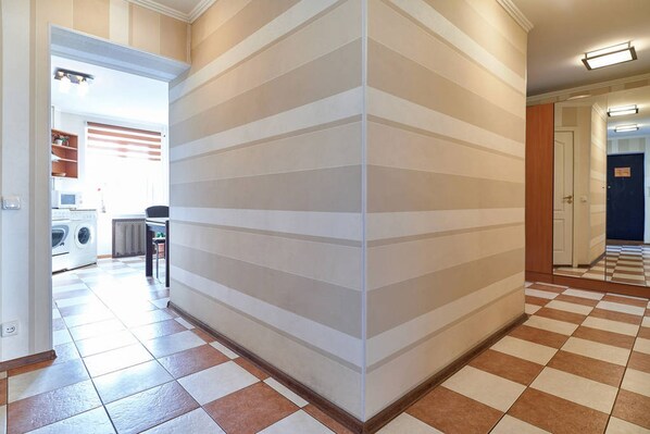 A hallway with a checkered floor, a corner with a striped wall, and a kitchen area visible in the background.