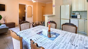 Een eethoek met een tafel bedekt met krantenprint, een decoratieve vaas en een klok. Er is een keuken met witte kasten en apparatuur.