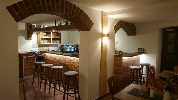 A cozy bar area with wooden stools, a counter with a television, and shelves with glasses and bottles. - Landgasthof Wetteraperle (Saalburg-Ebersdorf)