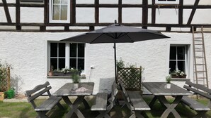 A wooden picnic table with a black umbrella, set against a white building with black timber framing. - Landgasthof Wetteraperle (Saalburg-Ebersdorf)