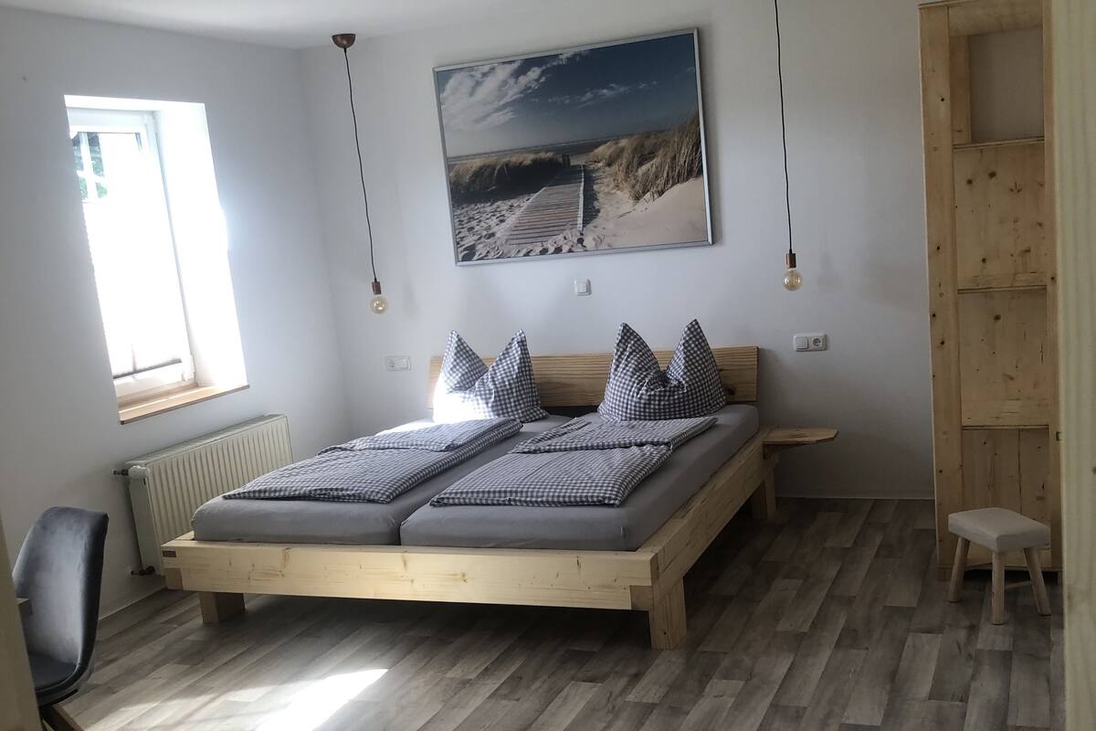 Une chambre avec un lit en bois, une fenêtre, un radiateur, un bureau et une étagère en bois.