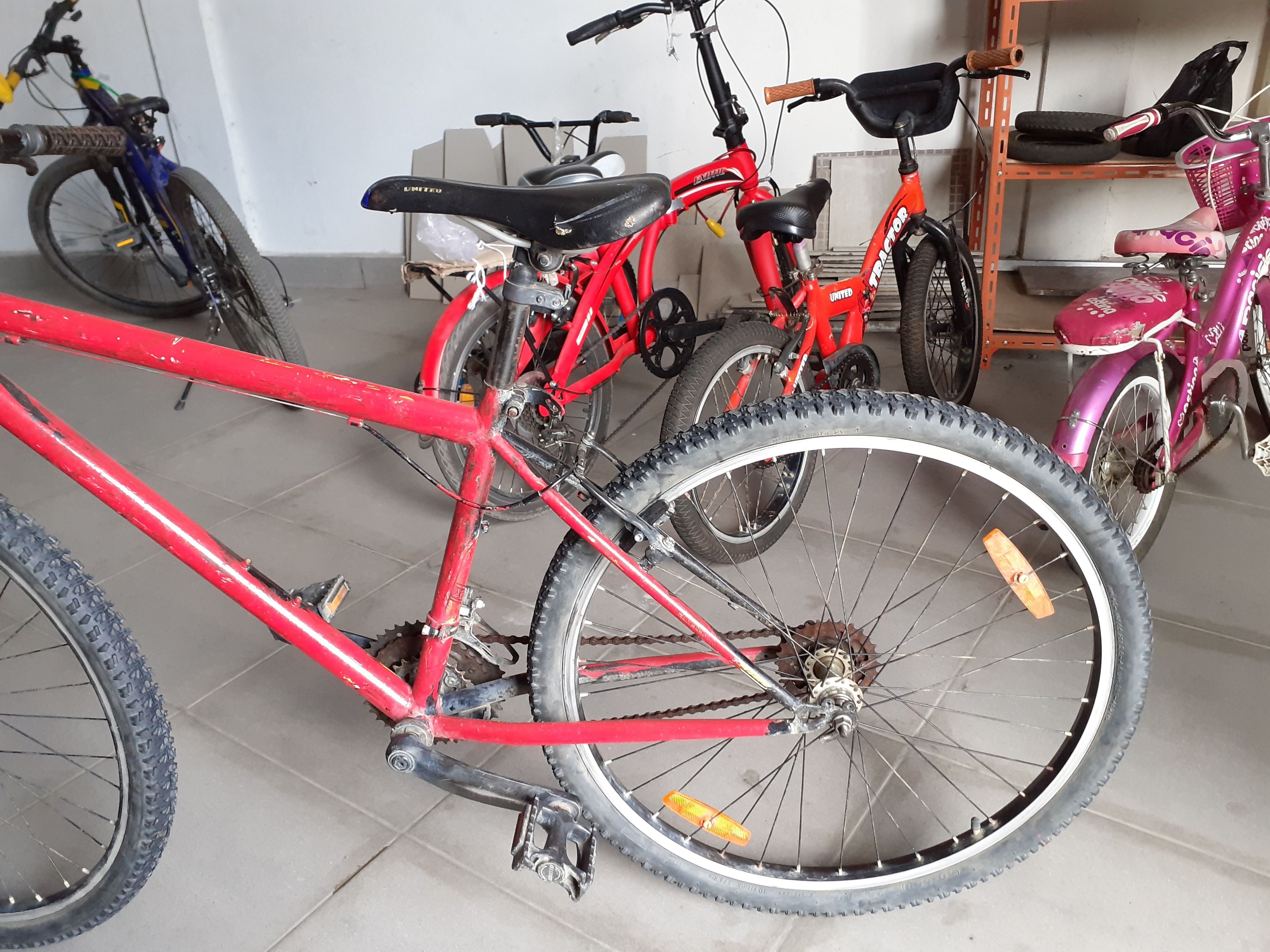 A bicycle with a red frame and black seat, parked indoors with other bicycles.