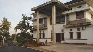 A two-story building with a concrete structure, multiple windows, and a paved driveway. - Almira Homestay (Jambi)