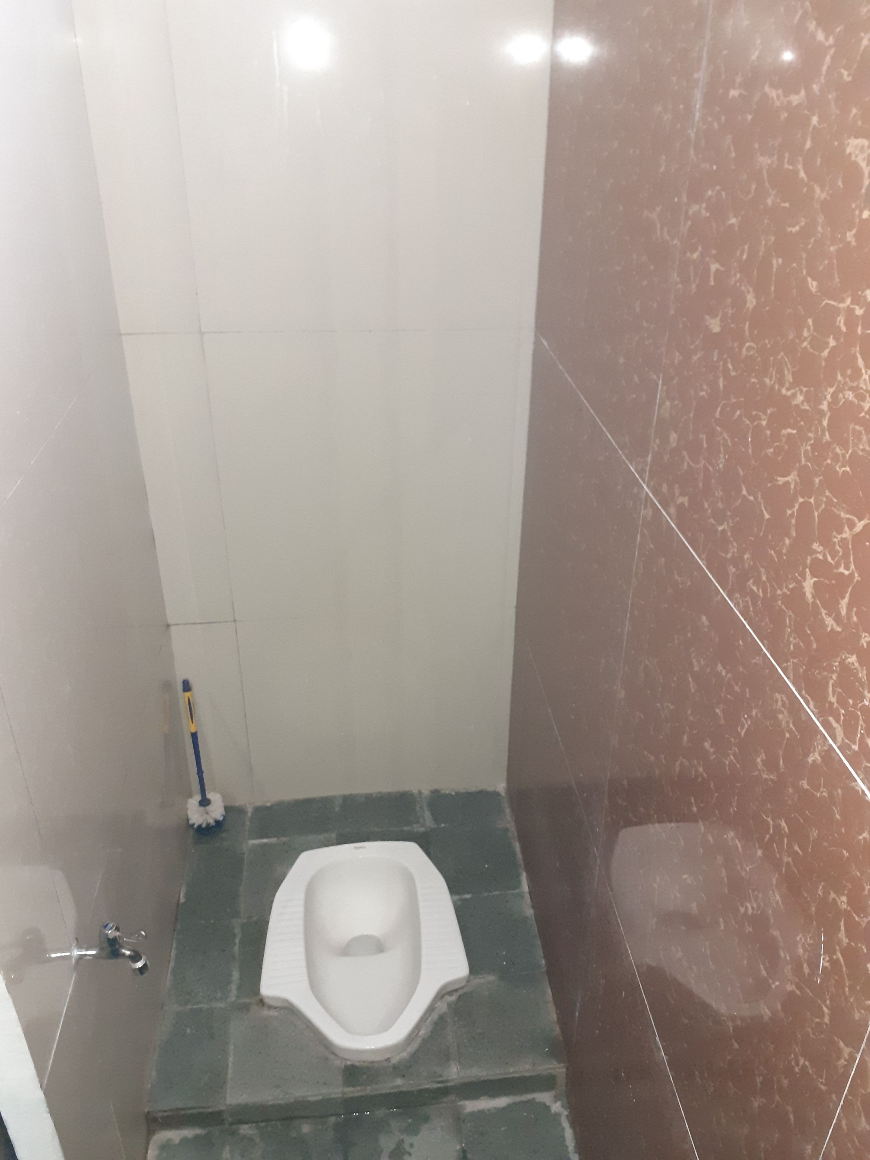 Une petite salle de bain privée, équipée de toilettes, d’un balai et d’une brosse pour les toilettes.